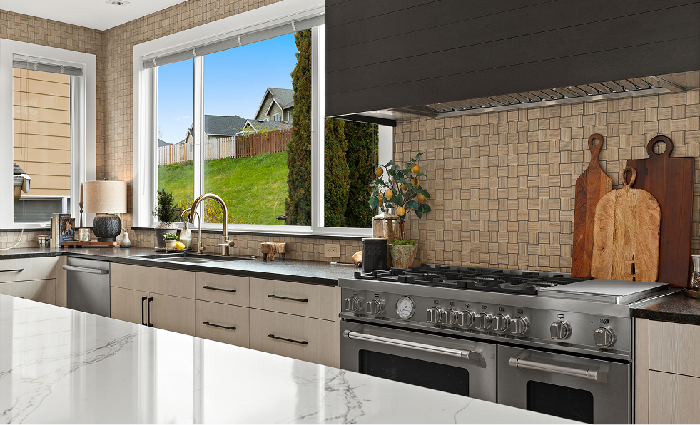 Modern kitchen with stainless appliances, large window, beige cabinets, and a sink overlooking a backyard.