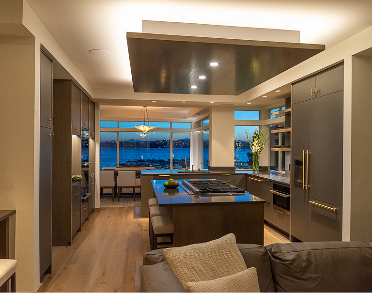 Modern kitchen with island, warm lighting, and ocean view at sunset