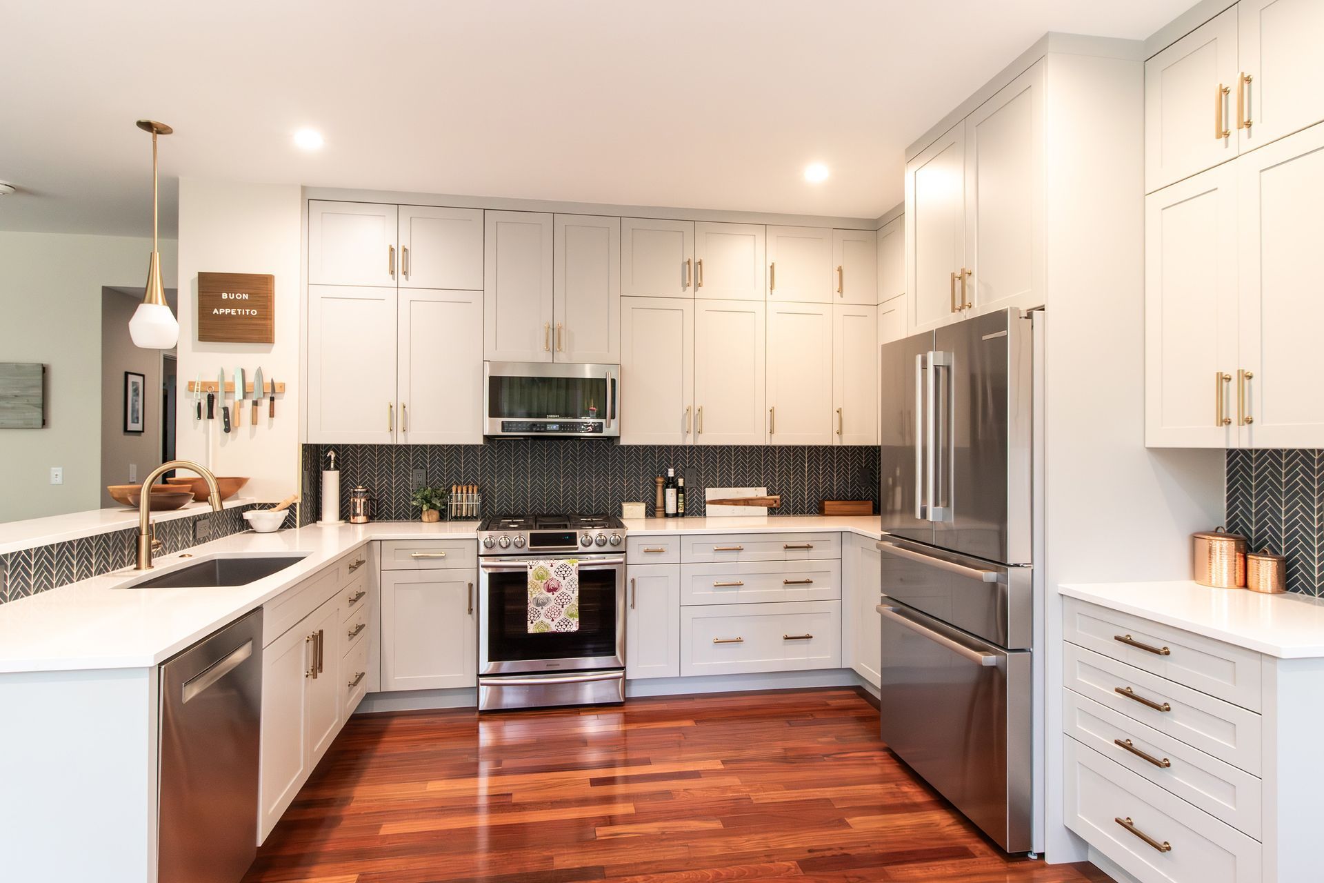 Bright modern kitchen with white cabinets, stainless steel appliances, dark backsplash, and wood floors