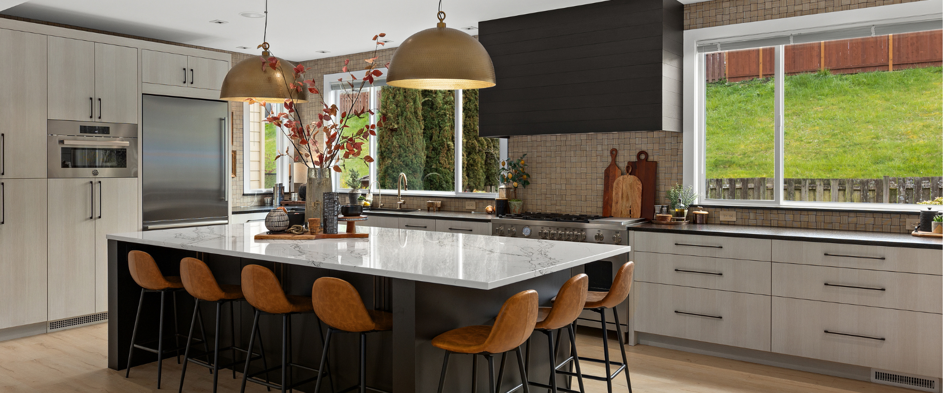 Bright modern kitchen with marble island, wooden stools, pendant lights, and large windows