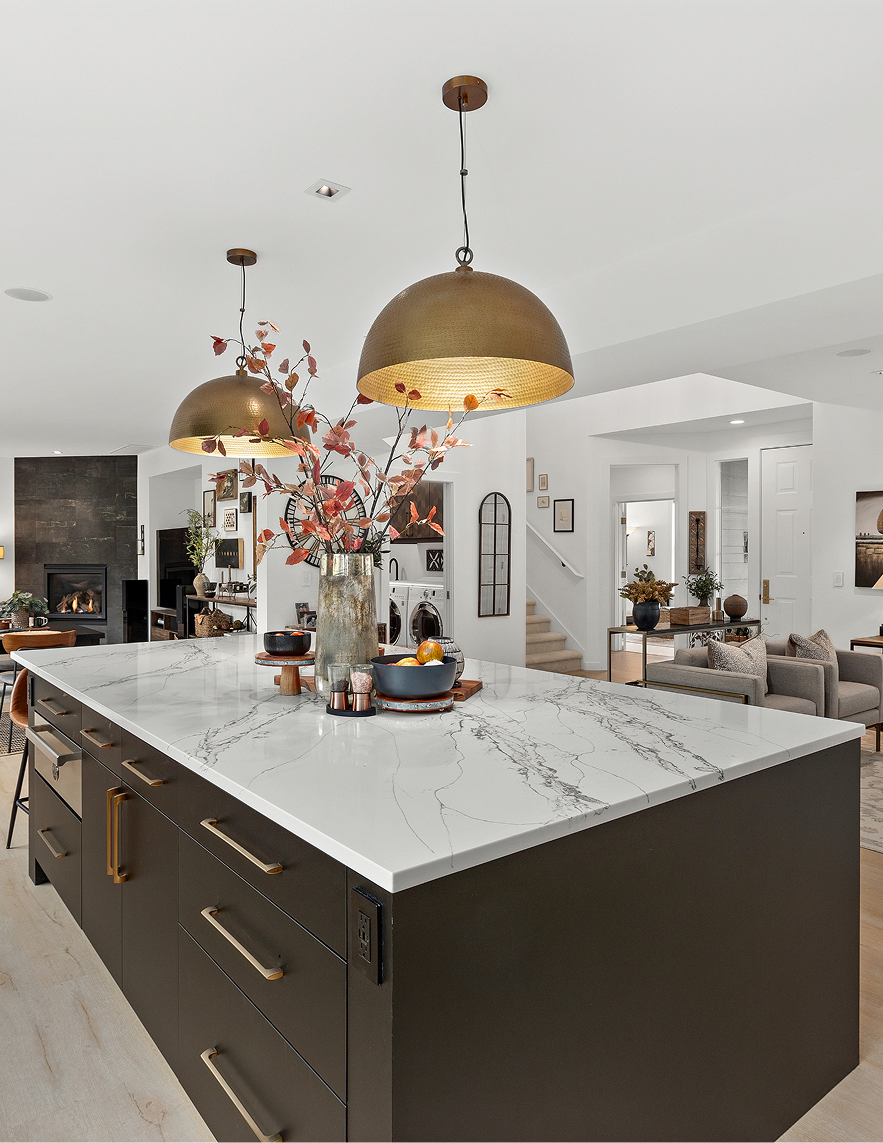 Modern kitchen with white island, gold pendant lights, and open living area beyond