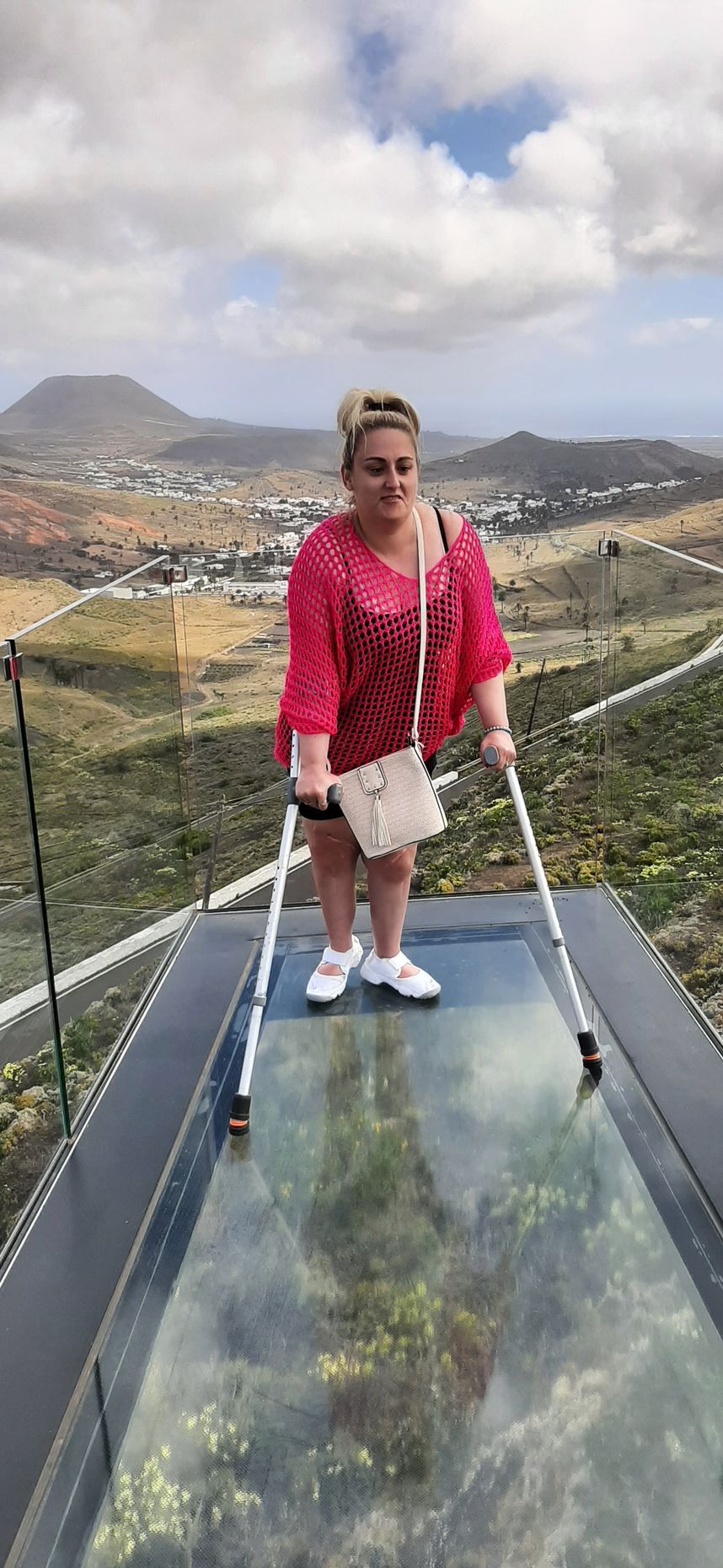 A woman with crutches is standing on a glass platform.