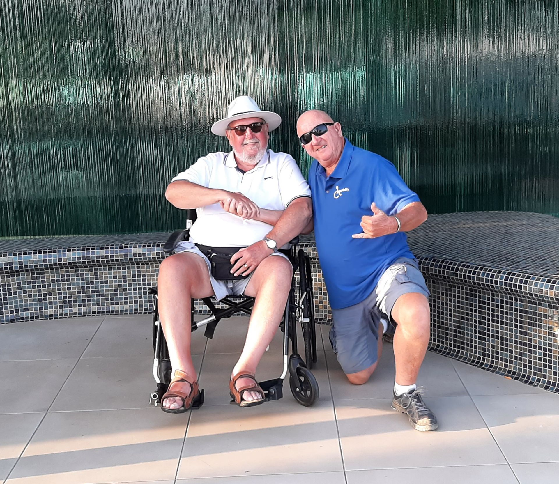 Two men are posing for a picture one is in a wheelchair