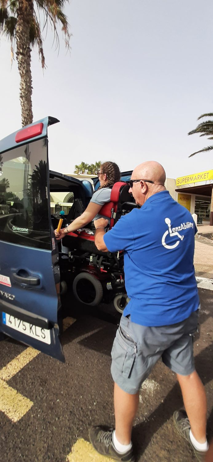 A man in a blue shirt is helping a woman in a wheelchair into a van.