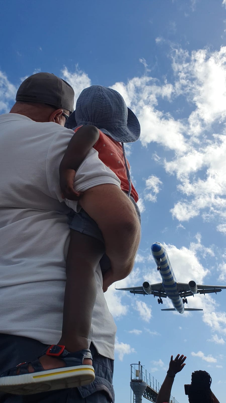 A man is holding a baby in his arms while watching a plane take off.