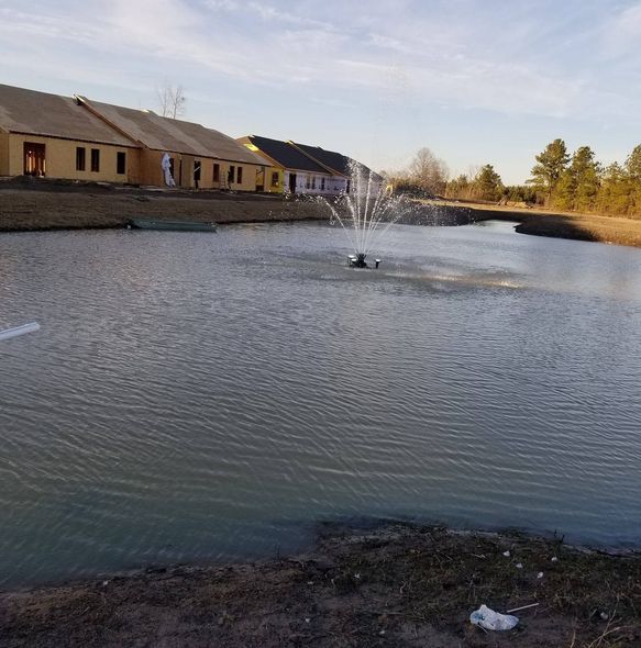 A pond with a fountain spraying water near houses at sunset