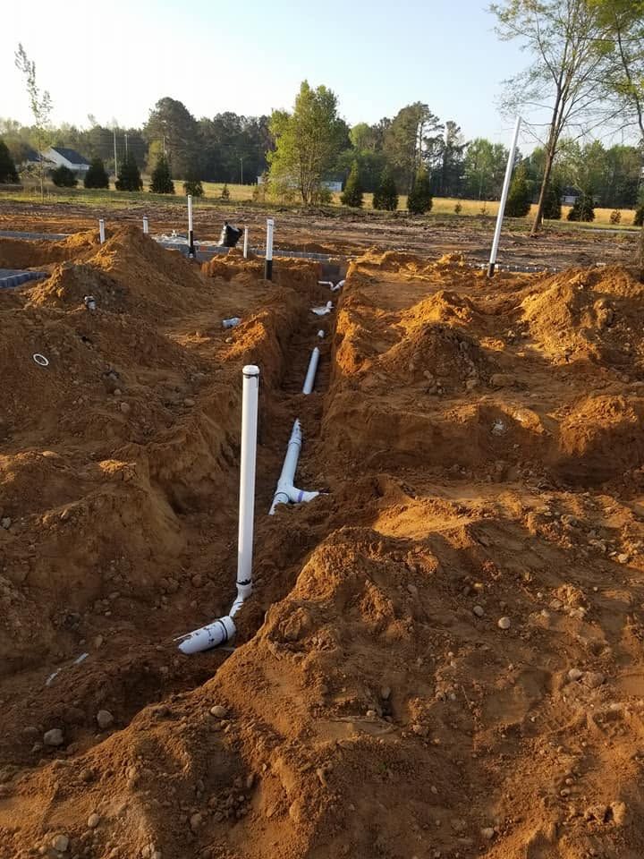 White PVC pipes trenching through reddish dirt at a construction site with trees in the background