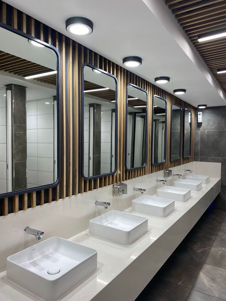 Modern restroom with row of white sinks, large mirrors, and wood-accented walls