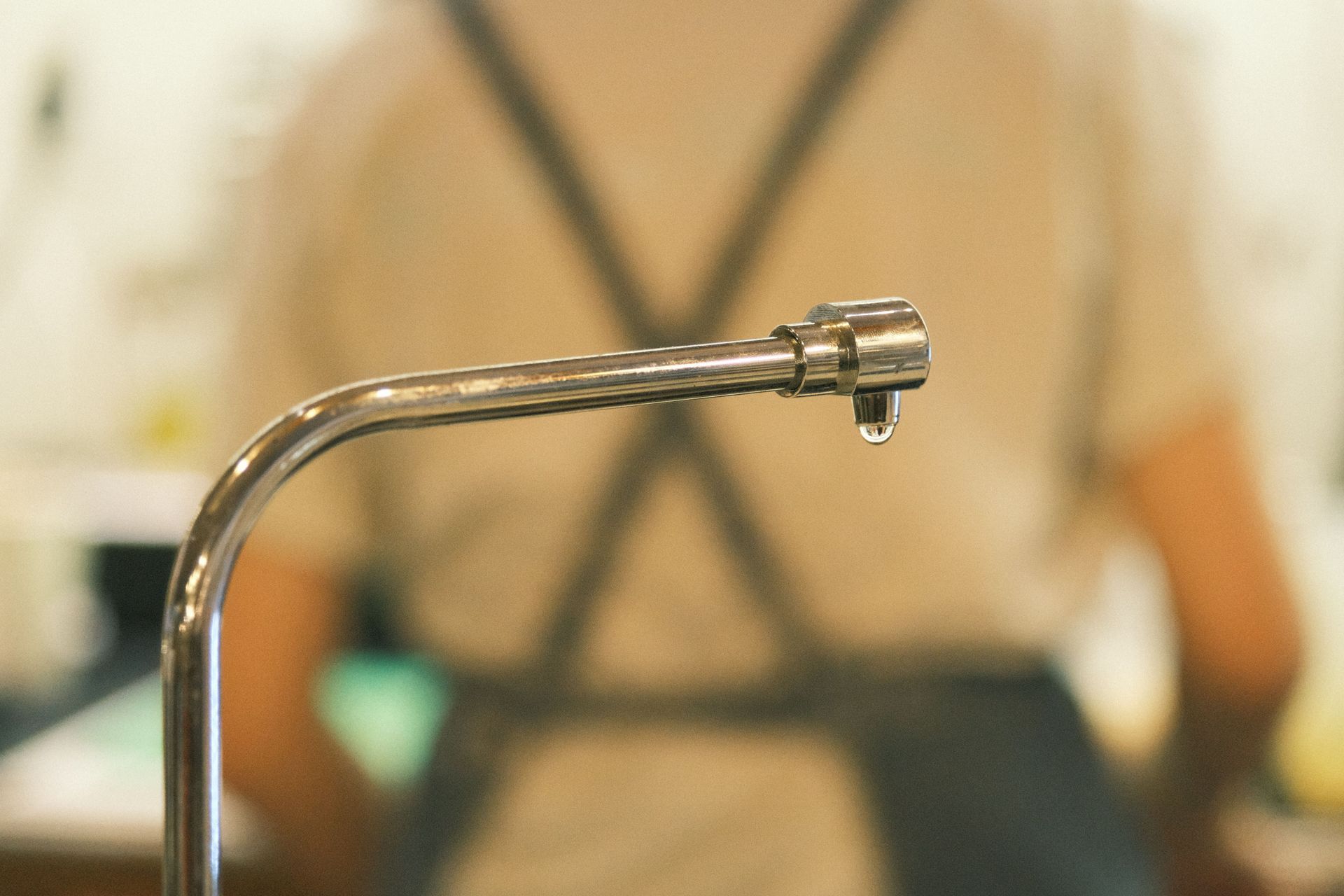 Chrome faucet spout in foreground, with a blurred person in a black apron behind it.