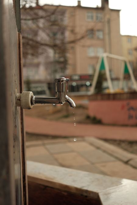 Close-up of a metal water tap with a blurred apartment courtyard in the background
