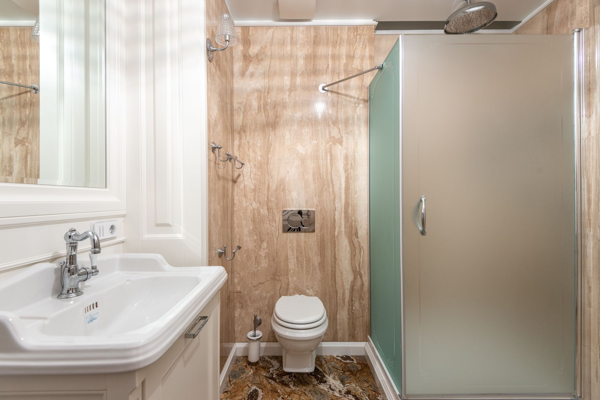 Small bathroom with white sink, toilet, marble shower walls, and frosted glass shower door