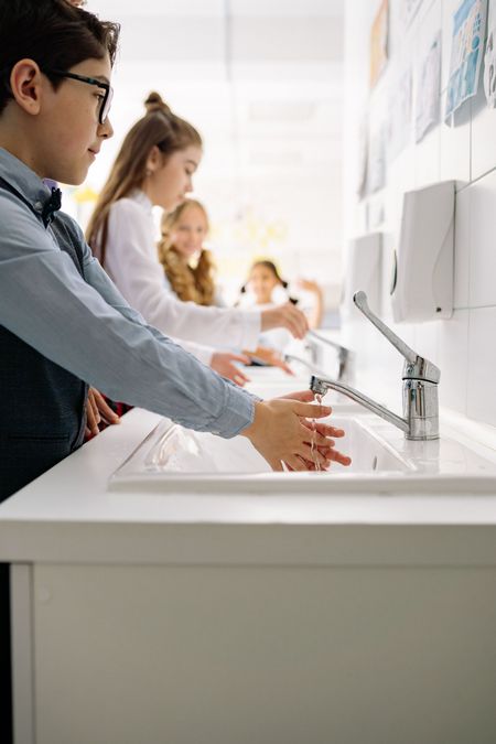 People washing hands at a row of white sinks in a bright restroom or lab