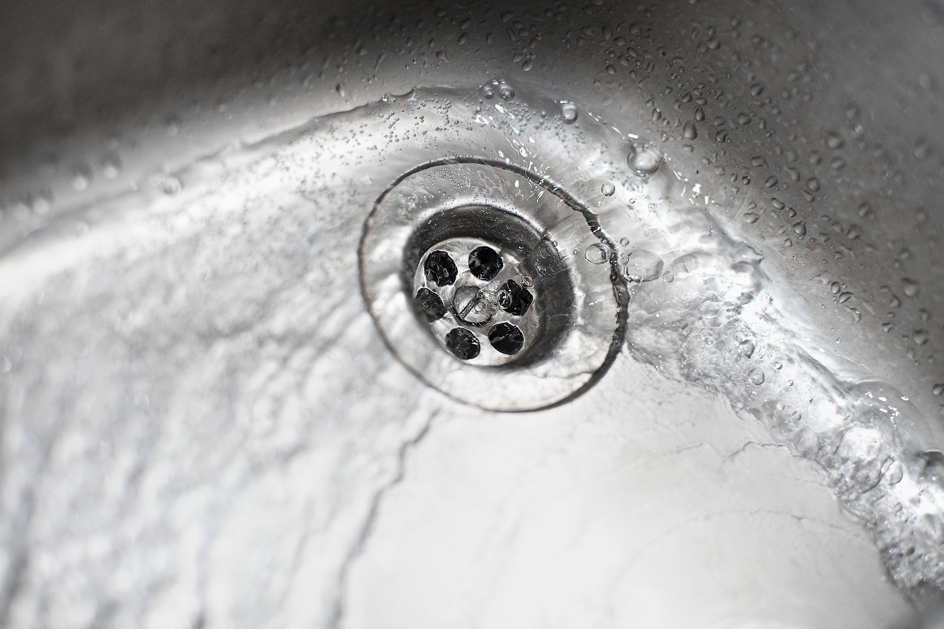 Close-up of a metal sink drain with a circular strainer and water droplets.