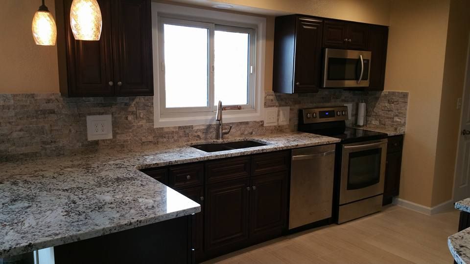 A bright, modern kitchen featuring white cabinets, gray wood-look flooring, a kitchen island, and a dining area window.