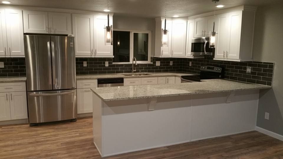 A modern kitchen featuring white cabinets, stainless steel appliances, speckled granite countertops, and a dark backsplash.