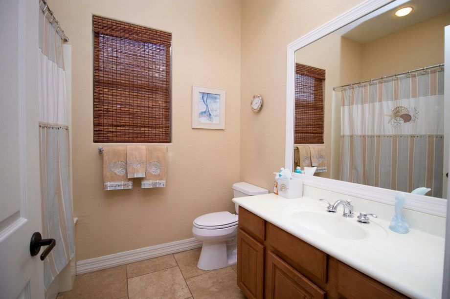 A bathroom with tan walls, a white vanity, a toilet, a tiled floor, a mirror, and a shower with a striped curtain.