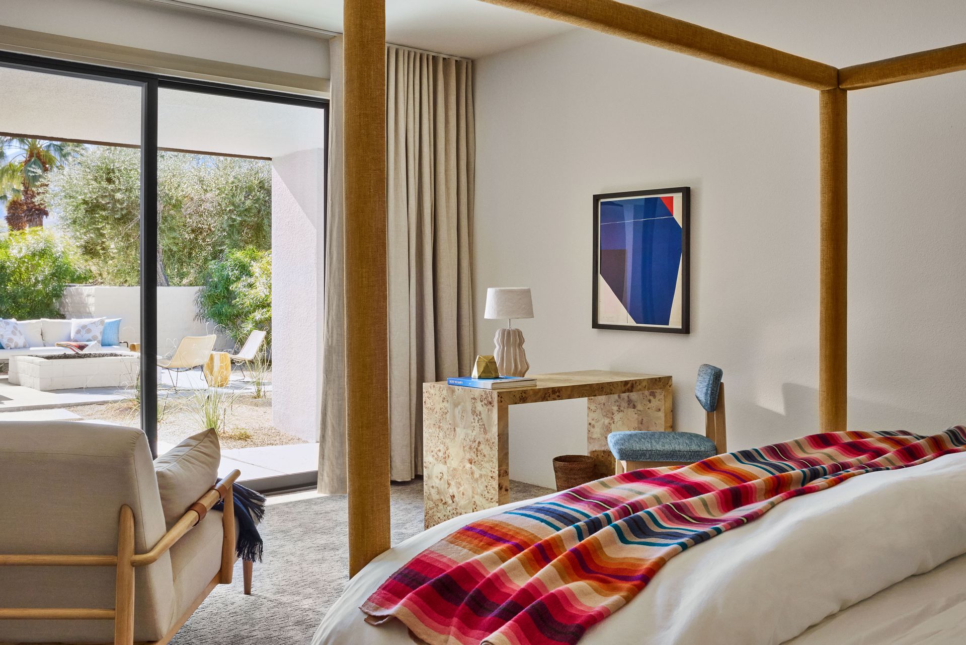 Bedroom with canopy bed, desk, and open door to outdoor patio with furniture and palm trees.