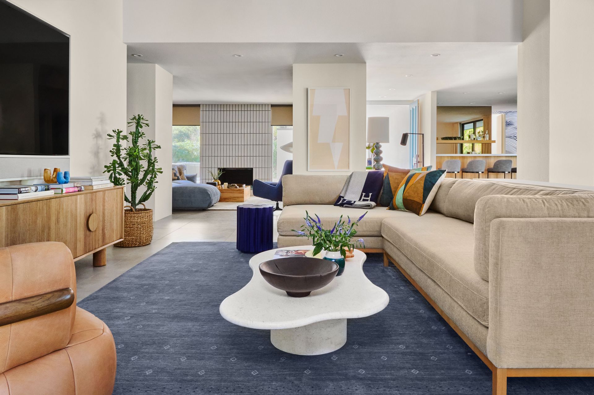 A modern living room with a beige sectional, blue rug, and a white coffee table.