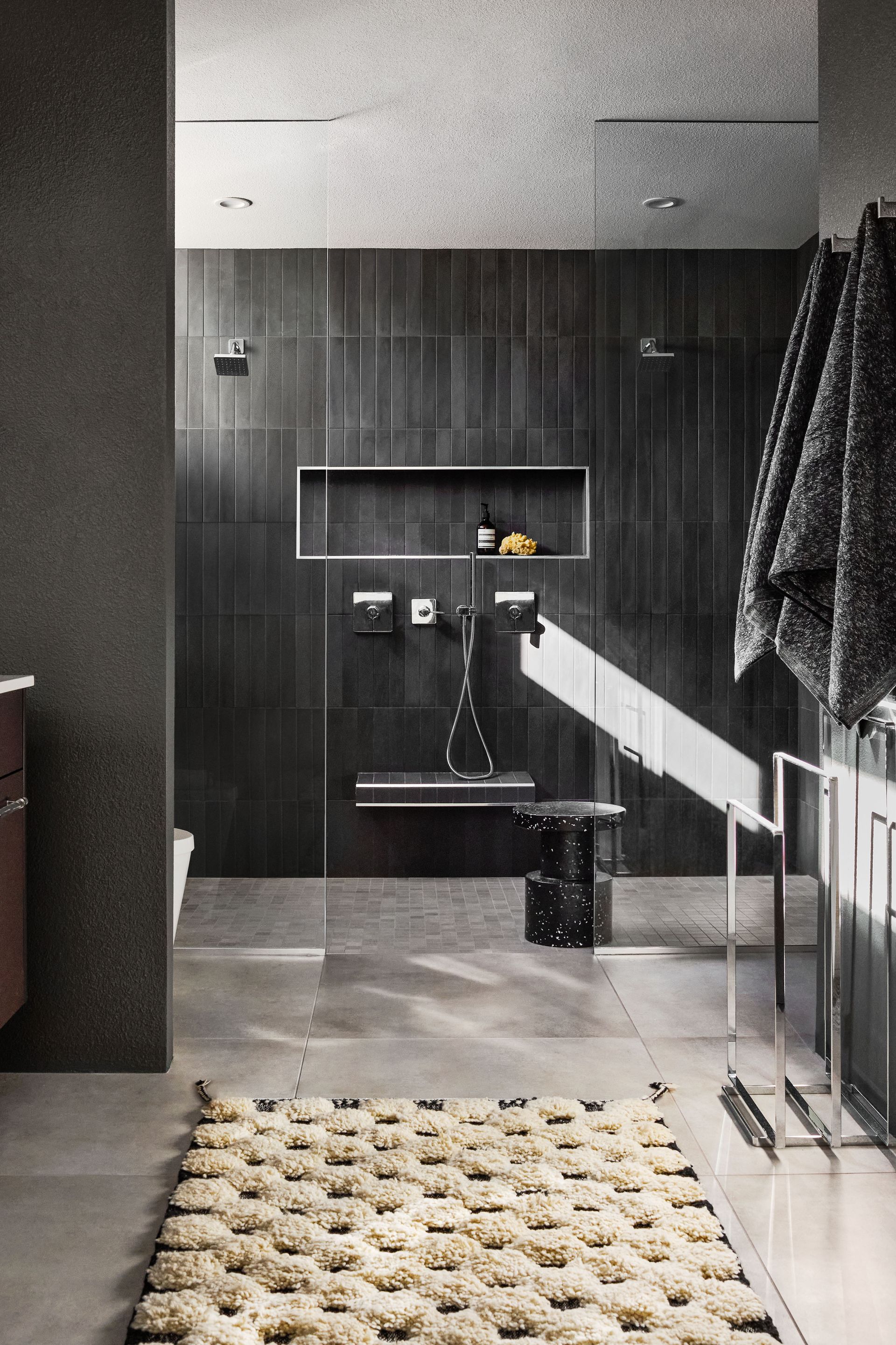 Modern bathroom with dark tile walls, a neutral rug, and a light beam.