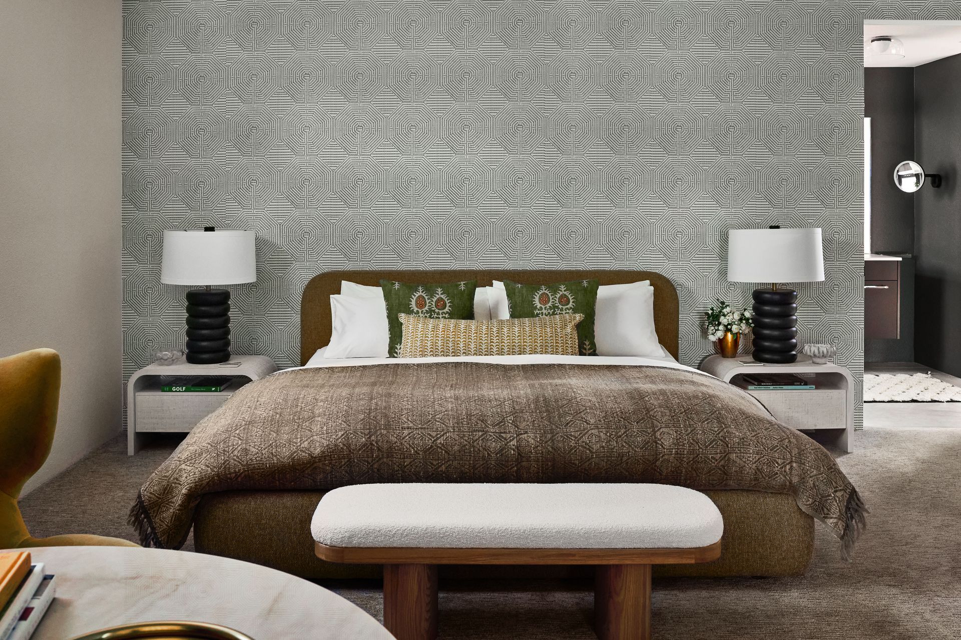 Bedroom with patterned wallpaper, bed, lamps, and a bench.