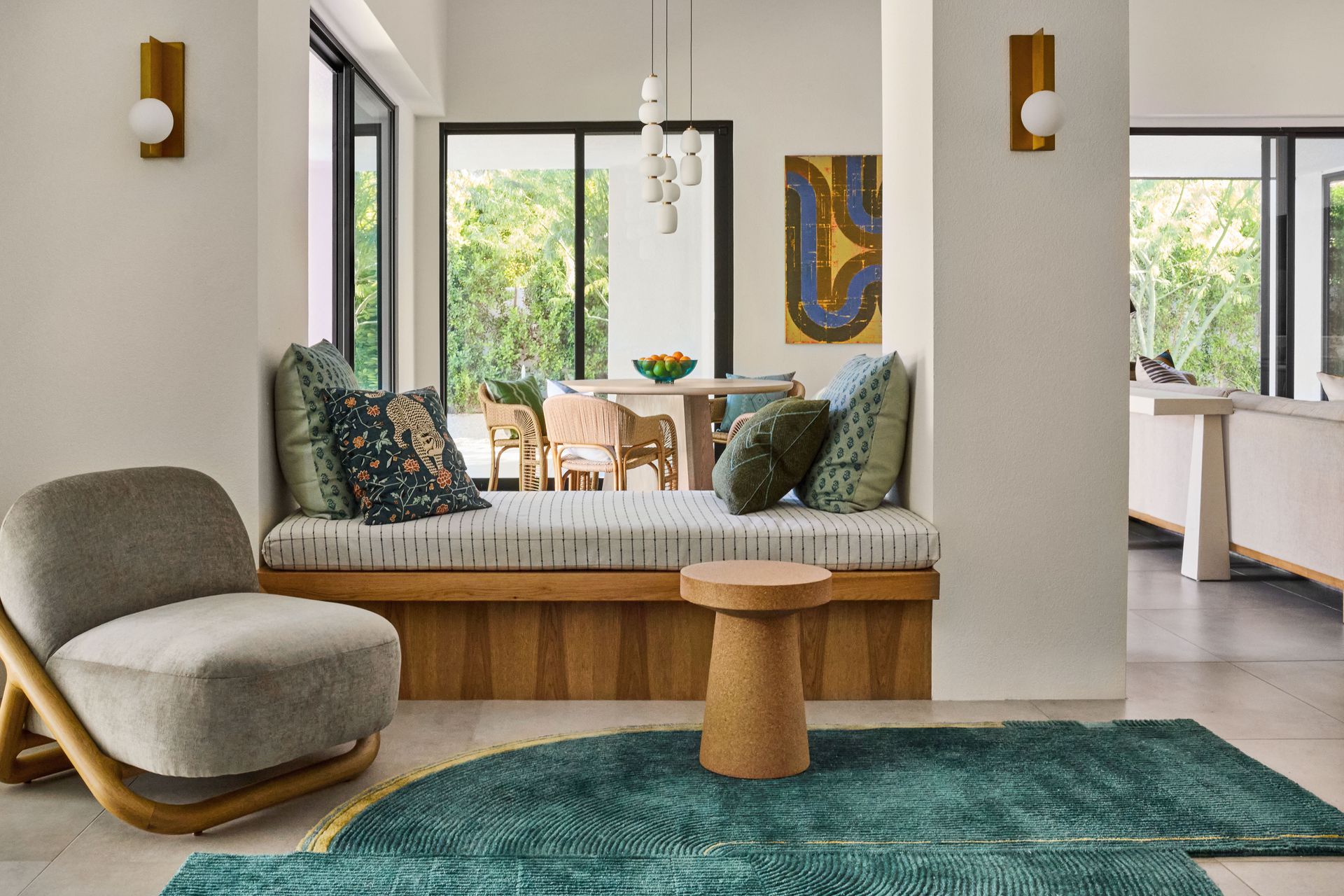 Cozy living space with a window seat, green rug, and wooden accents, featuring a chair and art piece.