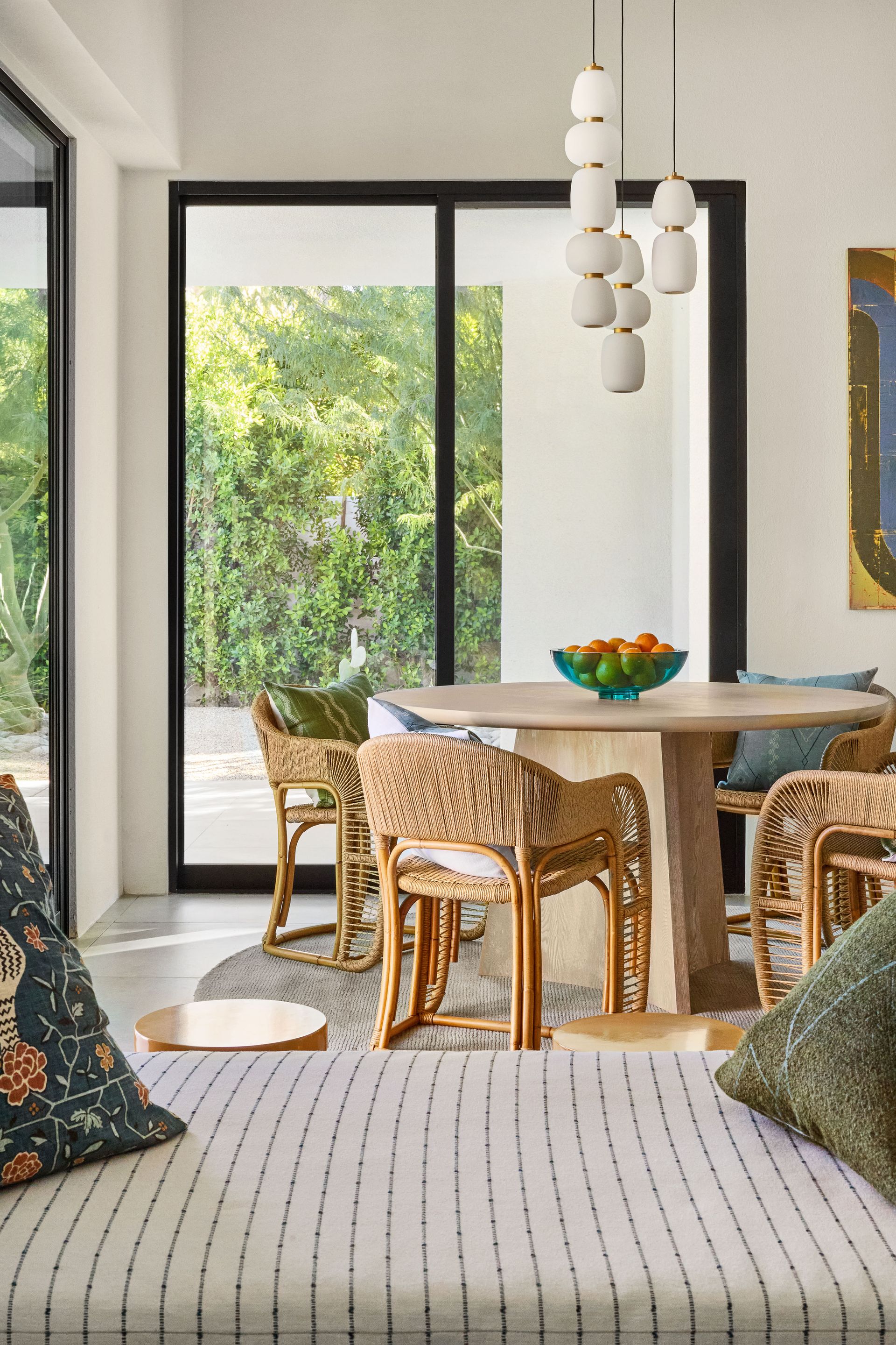 Dining area with round table, wicker chairs, and a view of greenery.