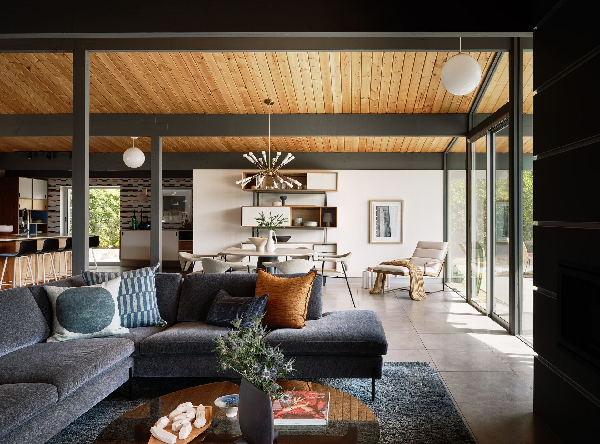 Living room with gray sectional, wooden ceiling, and large windows.