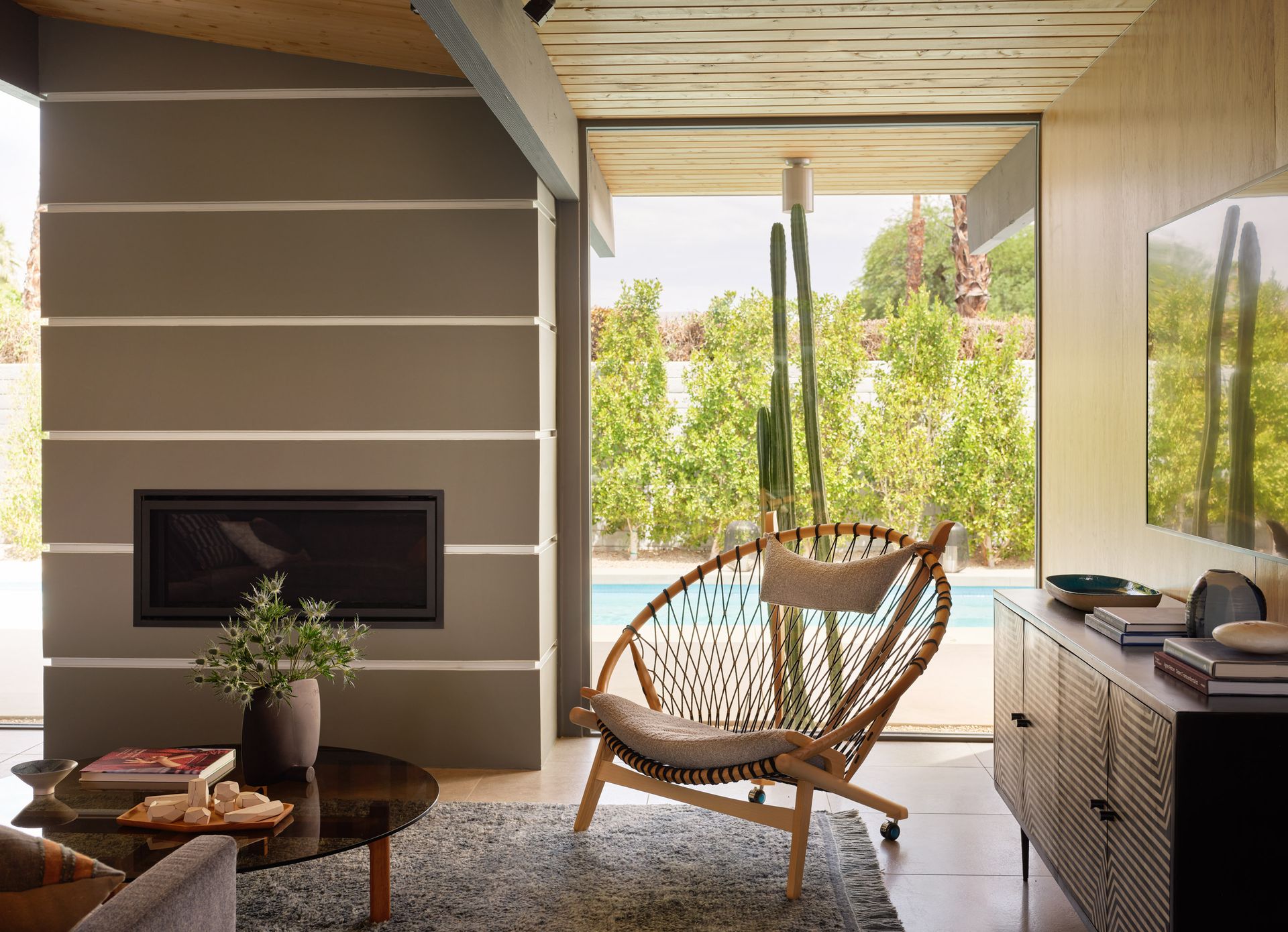 Living room with modern furniture, fireplace, large window with pool view, and cactus.
