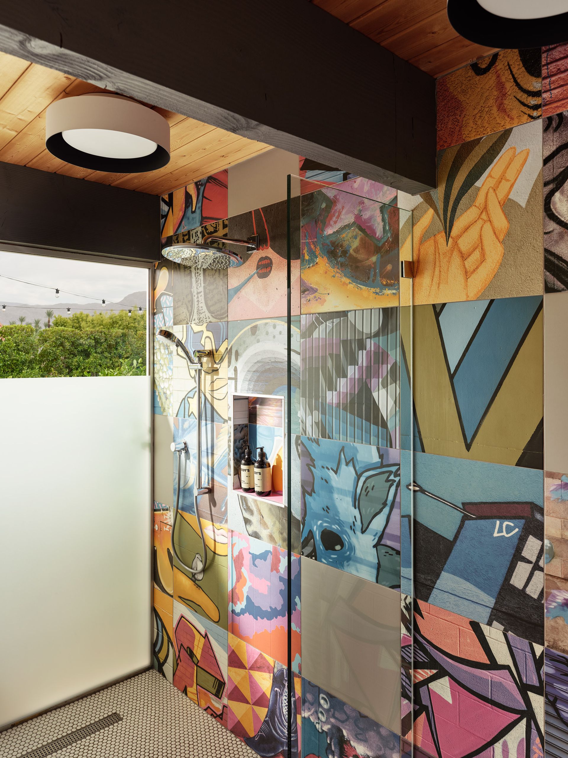 Shower with colorful patchwork walls, glass door, and rain showerhead; modern, artistic design.