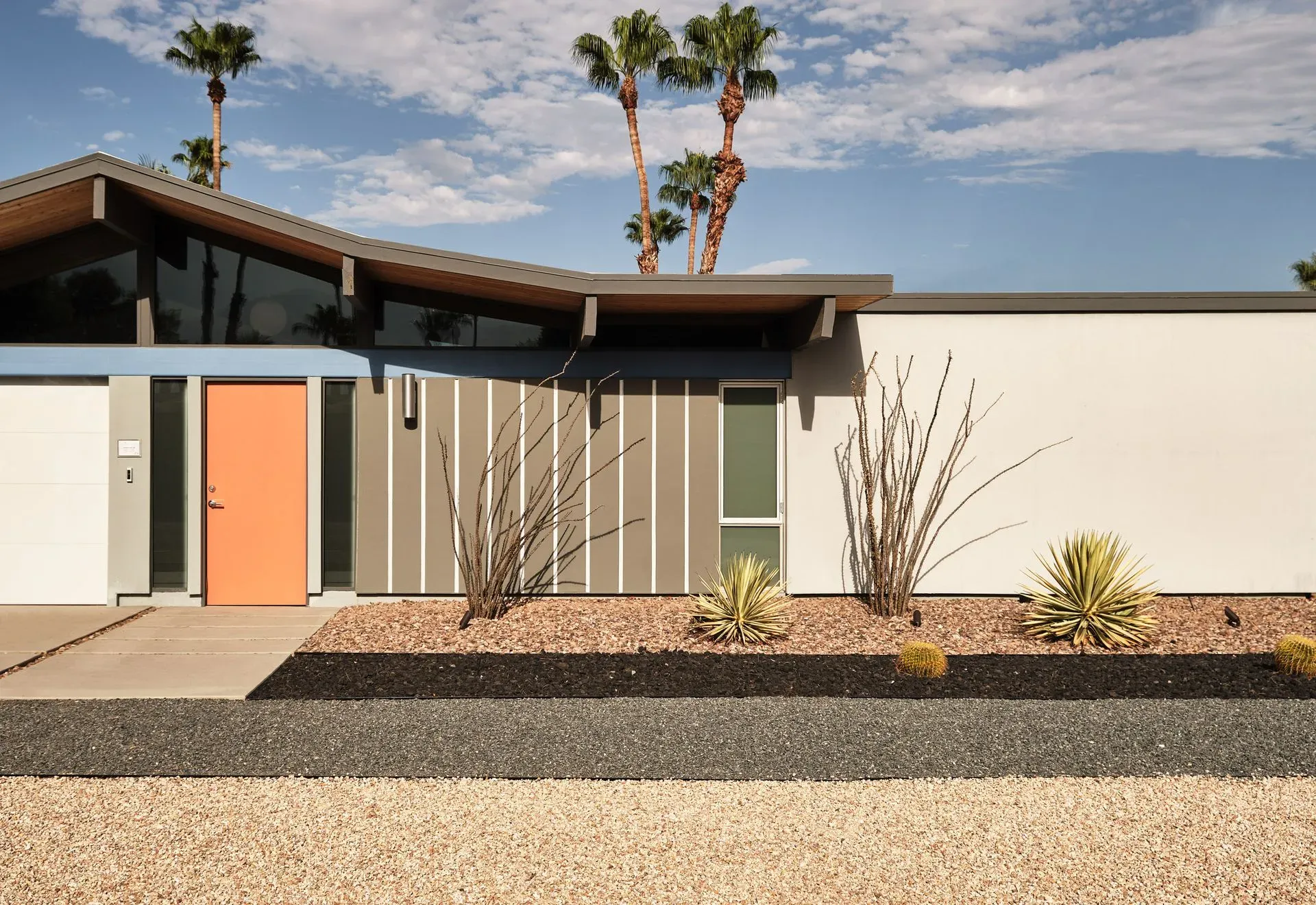 Modern home with orange door, grey siding, and palm trees.