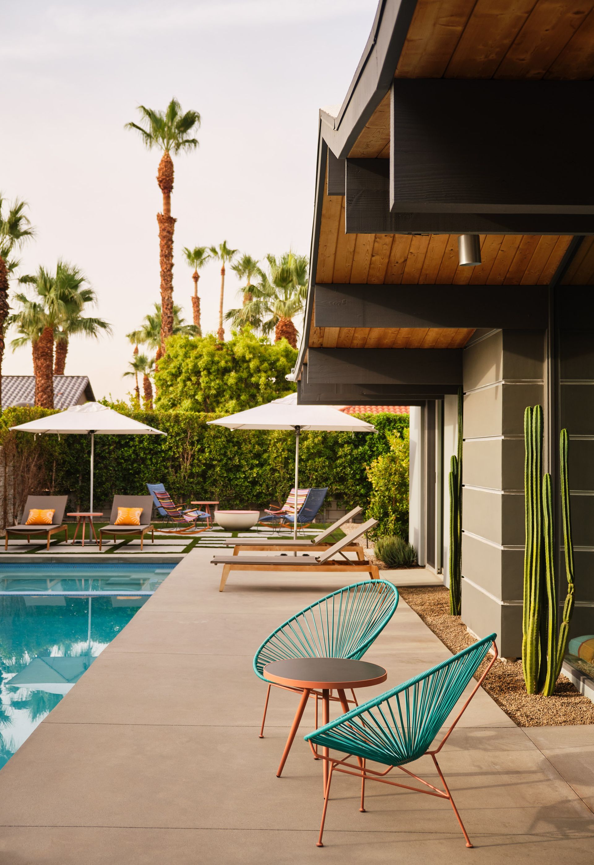 Poolside scene with turquoise chairs, lounge chairs, and palm trees.
