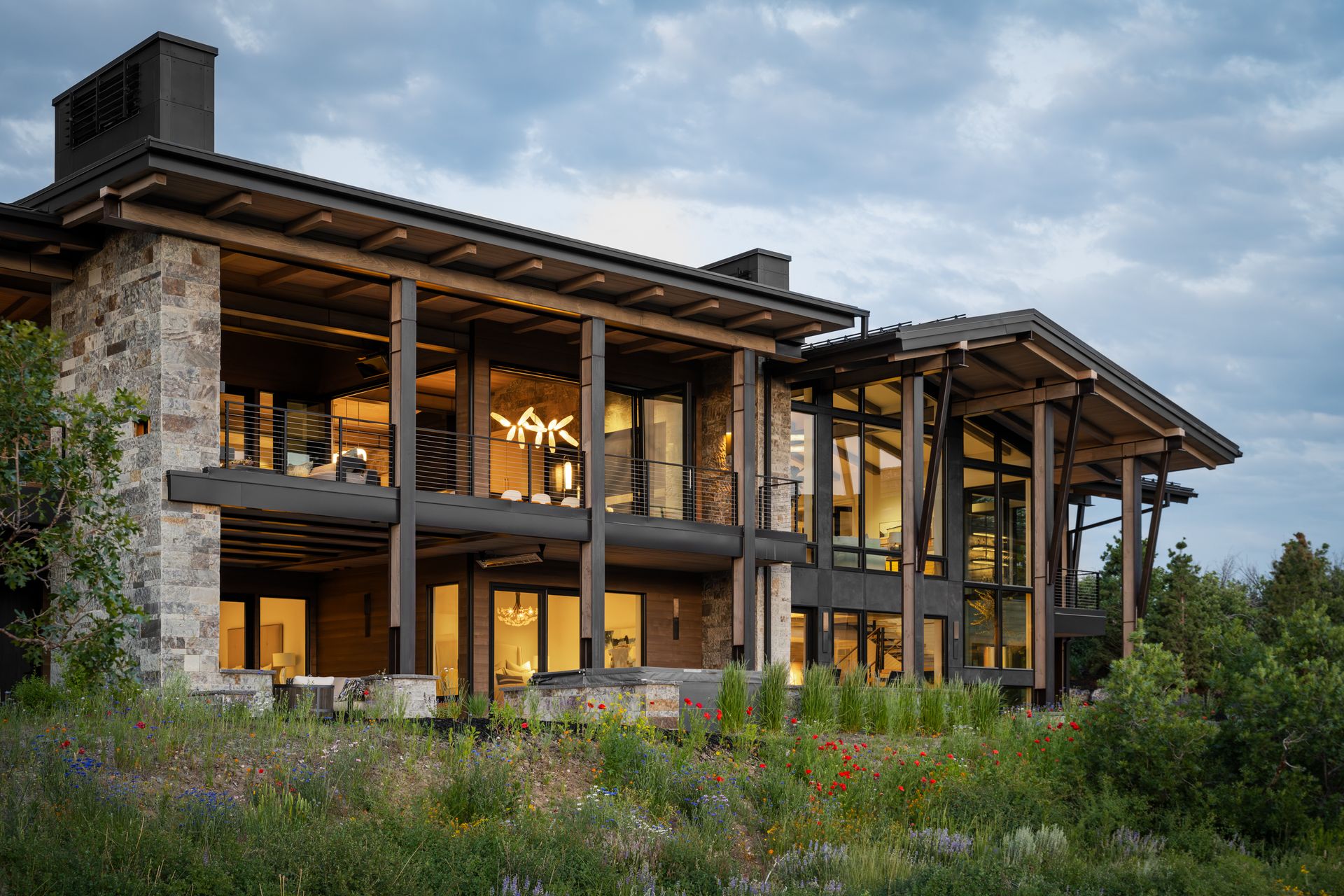 Modern house with stone walls, large windows, and exposed wooden beams at dusk.