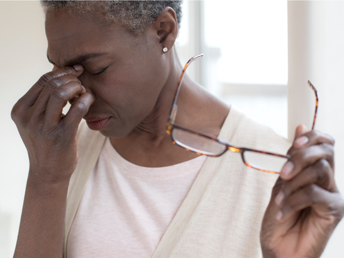 An older woman is holding her glasses and rubbing her nose.