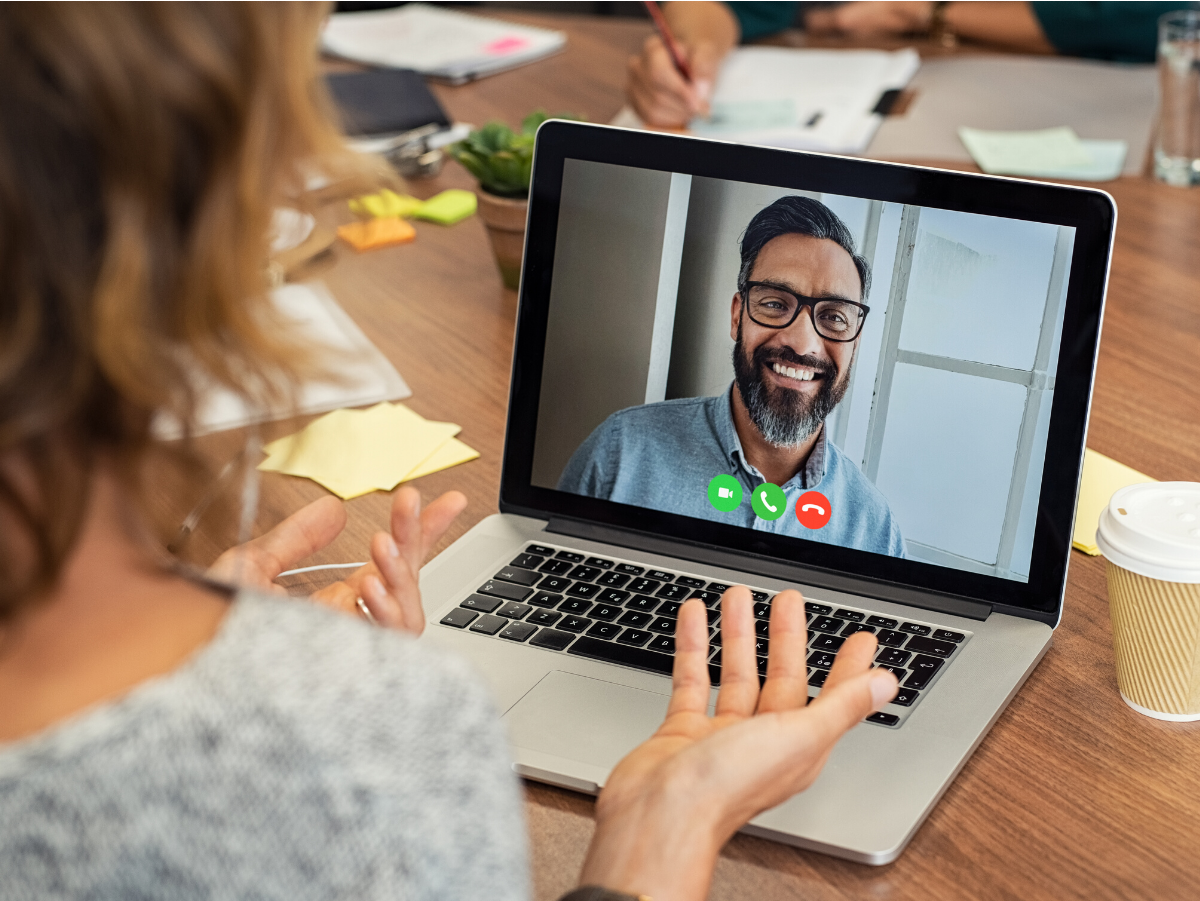 A woman is sitting at a table using a laptop computer to have a video call with a man.