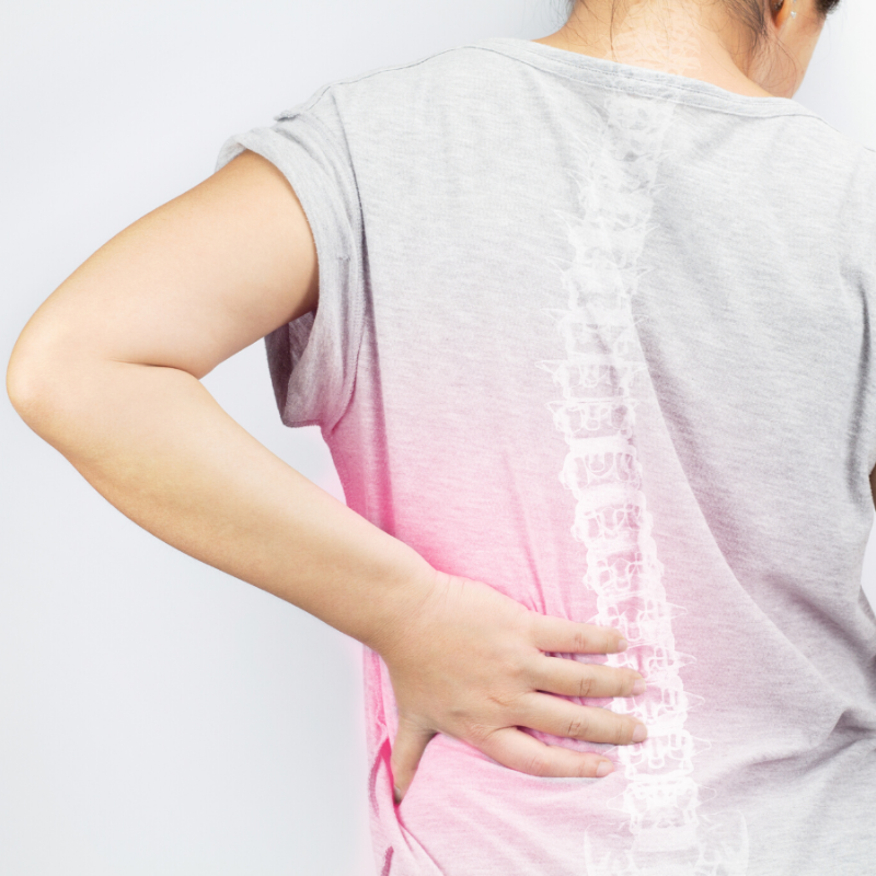 A woman in a pink shirt is holding her back in pain.