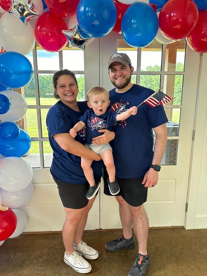 A man and woman are holding a baby in front of balloons.