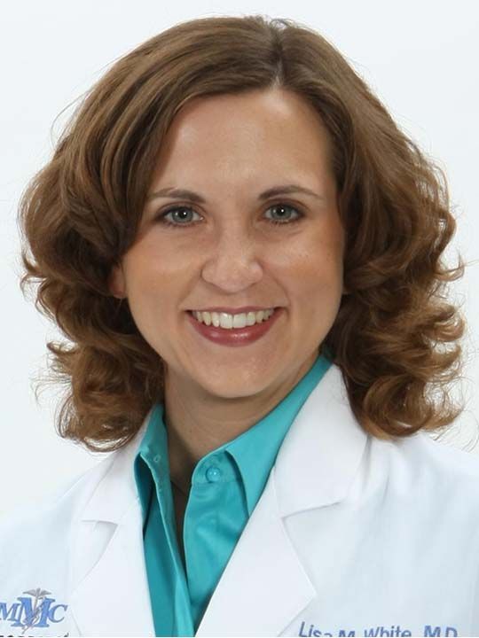 A woman in a white lab coat is smiling for the camera