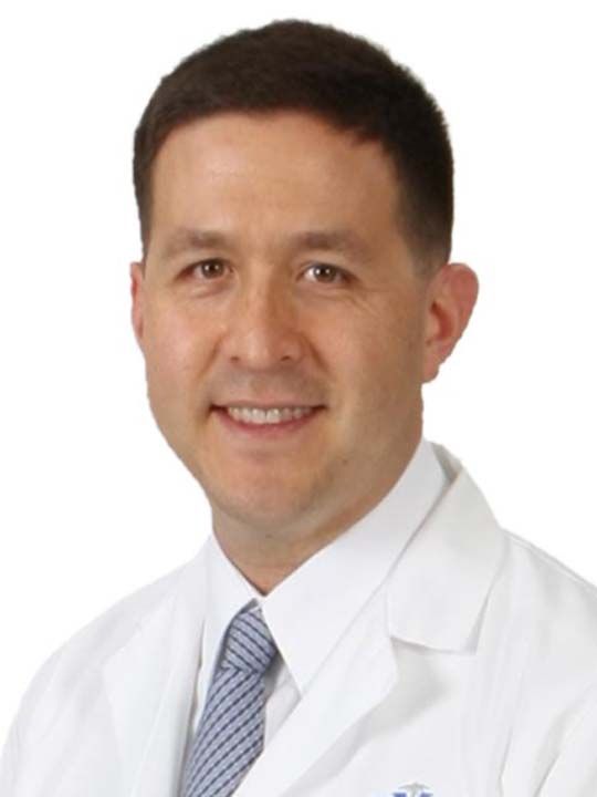 A man in a white coat and tie smiles for the camera