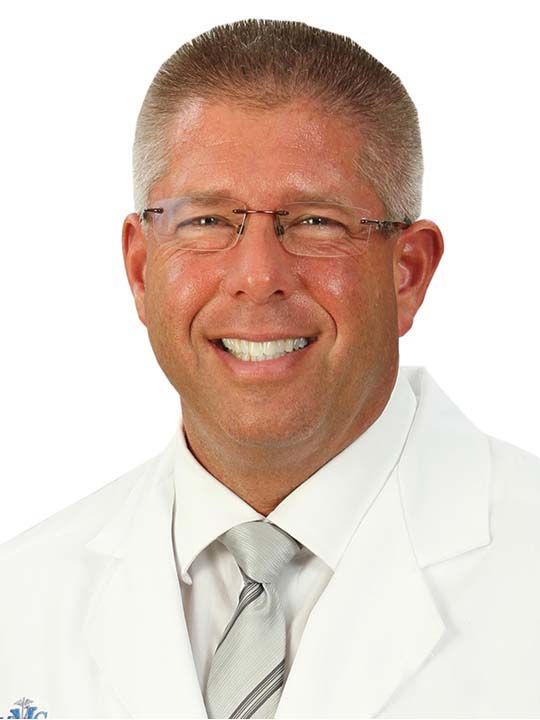 A man in a white coat and tie smiles for the camera