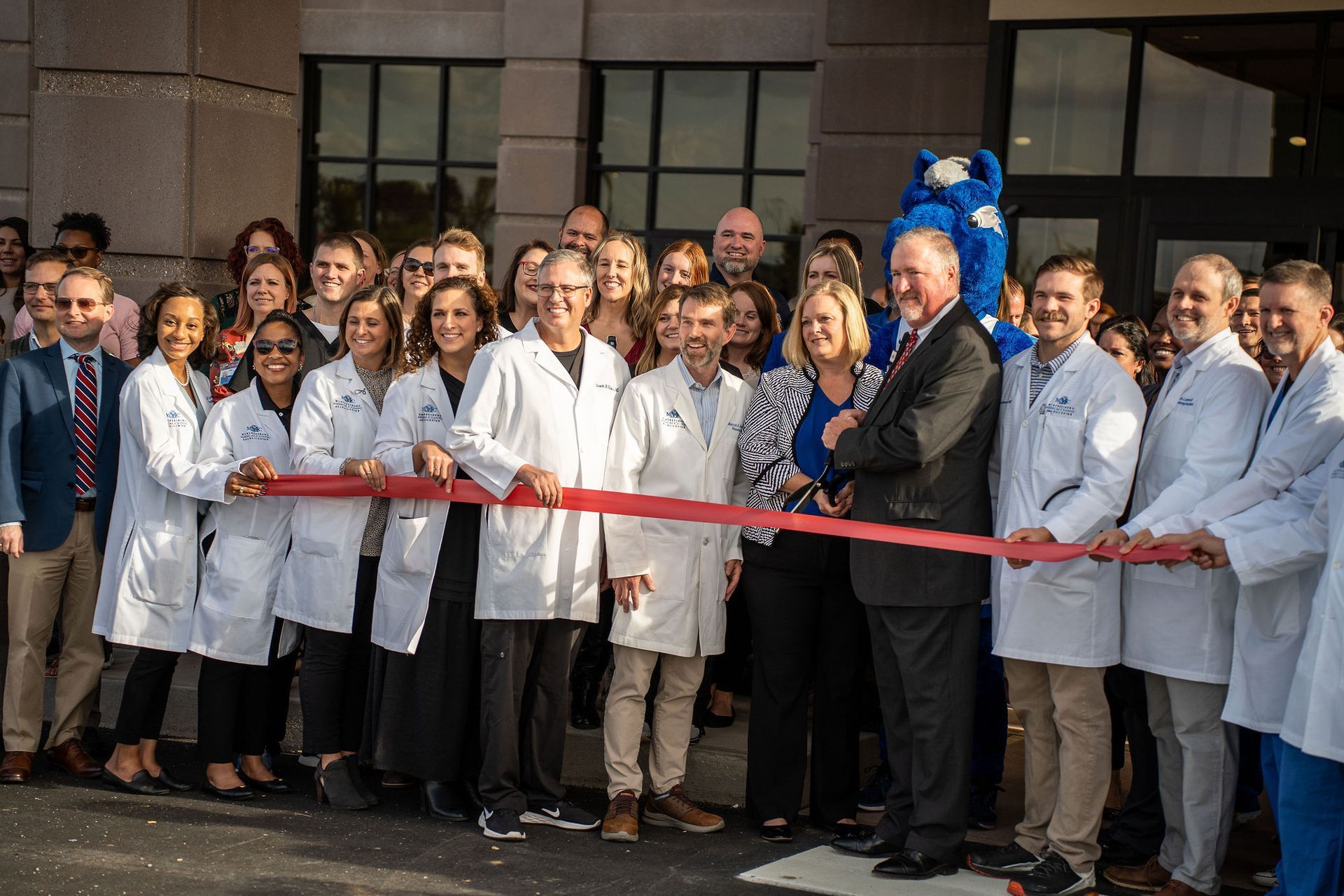A group of doctors and nurses are cutting a red ribbon.