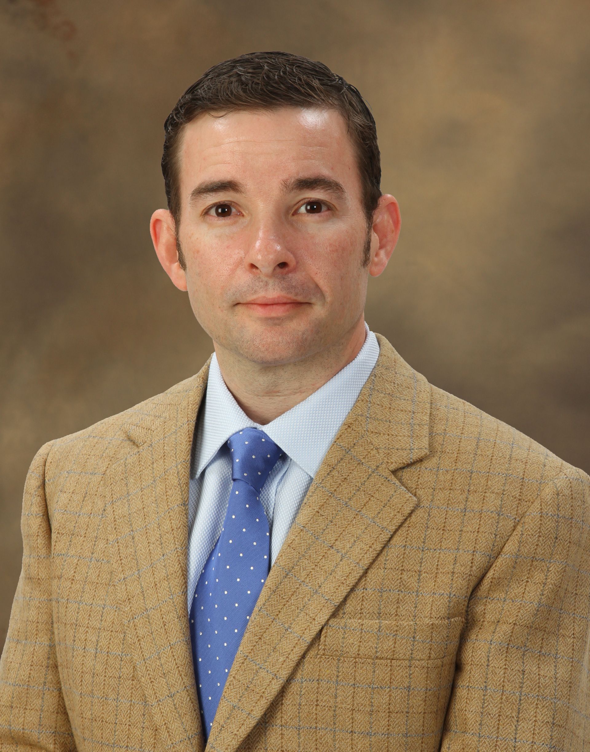 A man in a suit and tie stands in front of a brown background