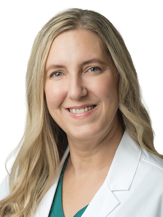 A woman in a white lab coat with a stethoscope around her neck is smiling.
