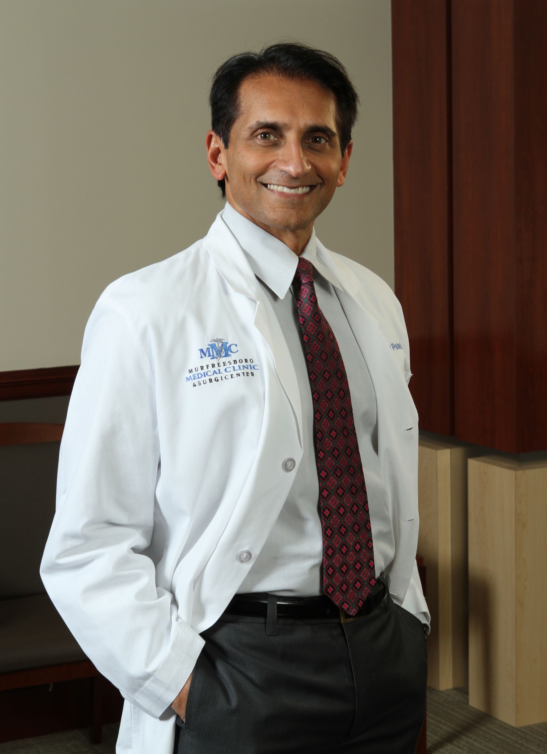 A man in a lab coat and tie is smiling for the camera