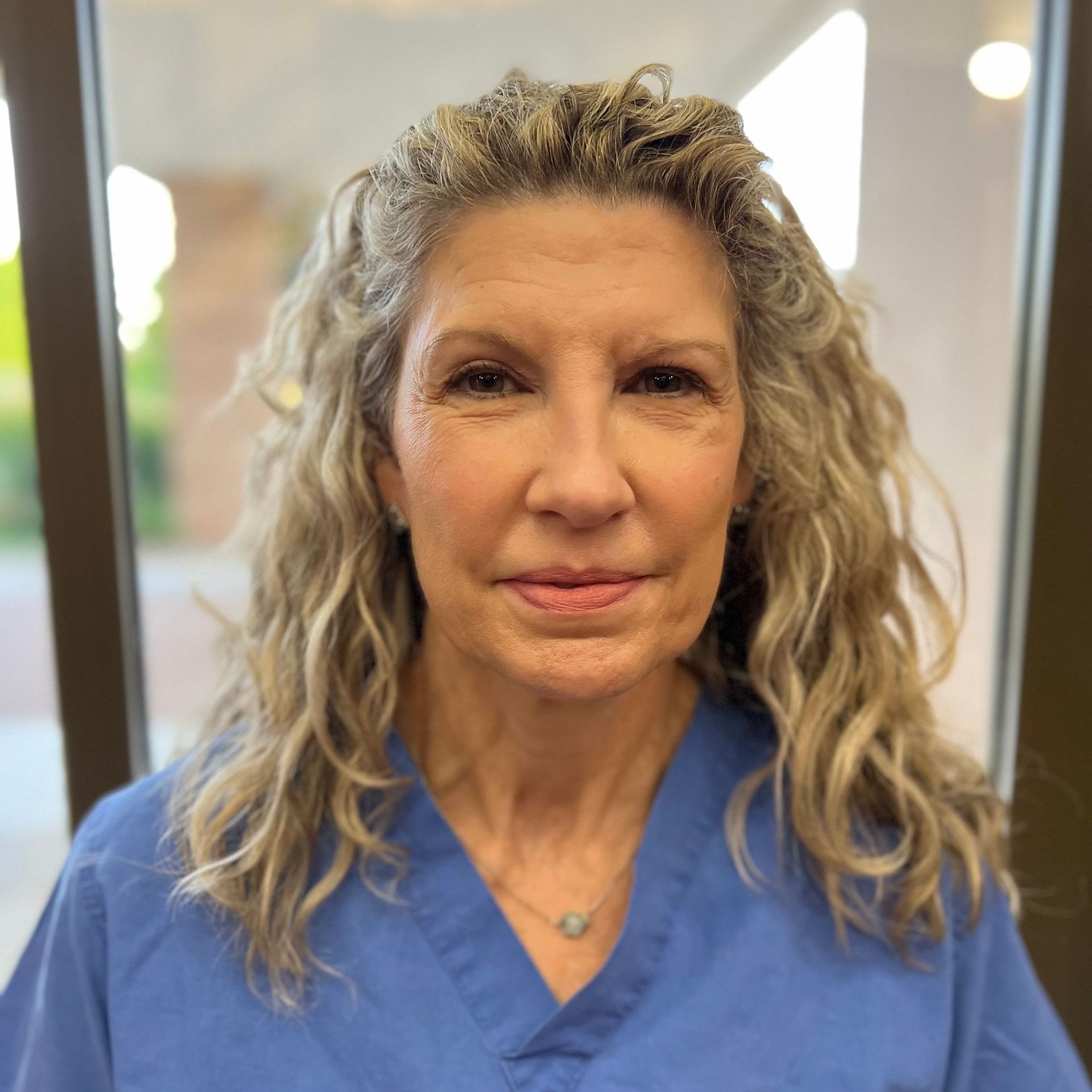 A woman wearing  a blue scrub top smiles for the camera.