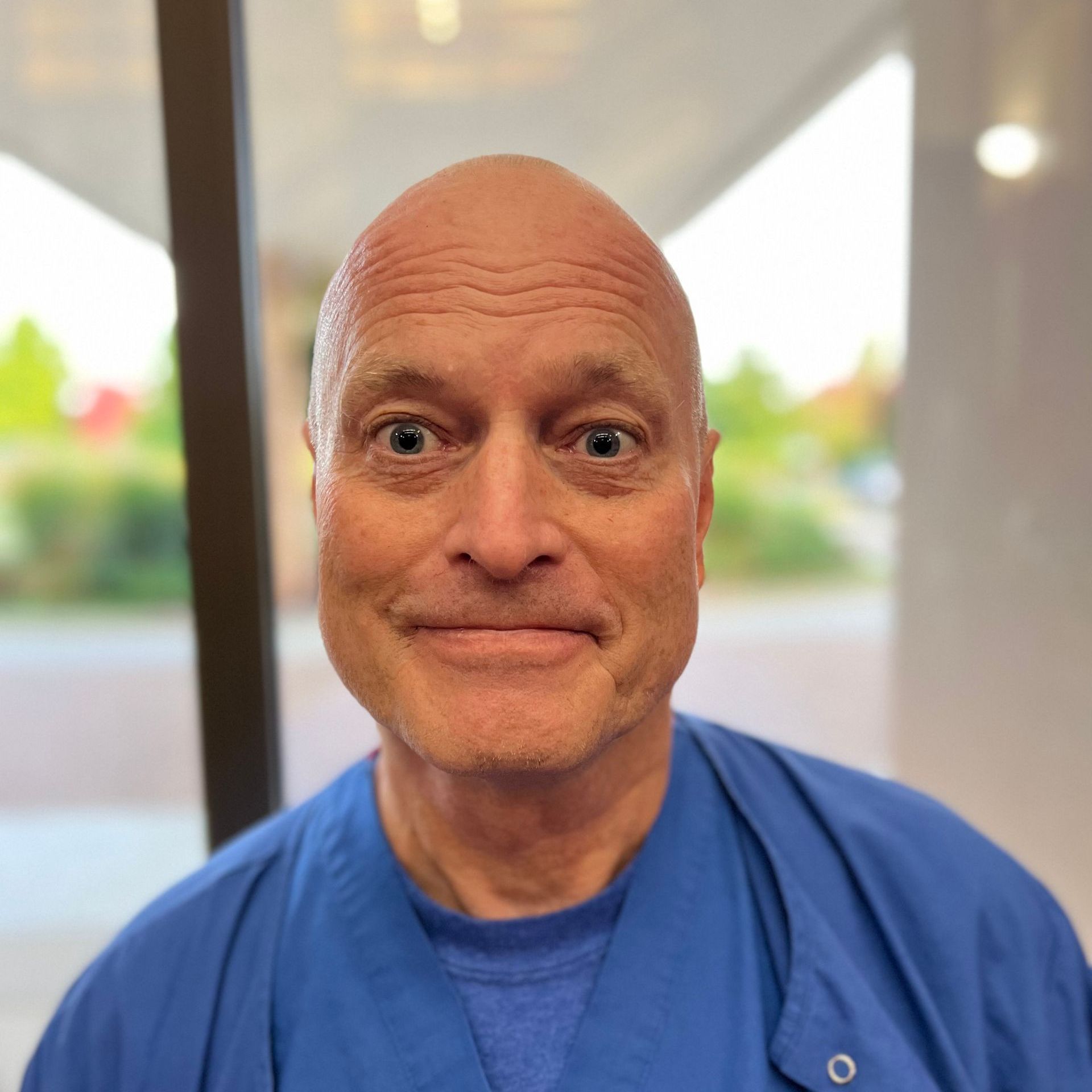A man with a beard and glasses is wearing a blue scrub top.