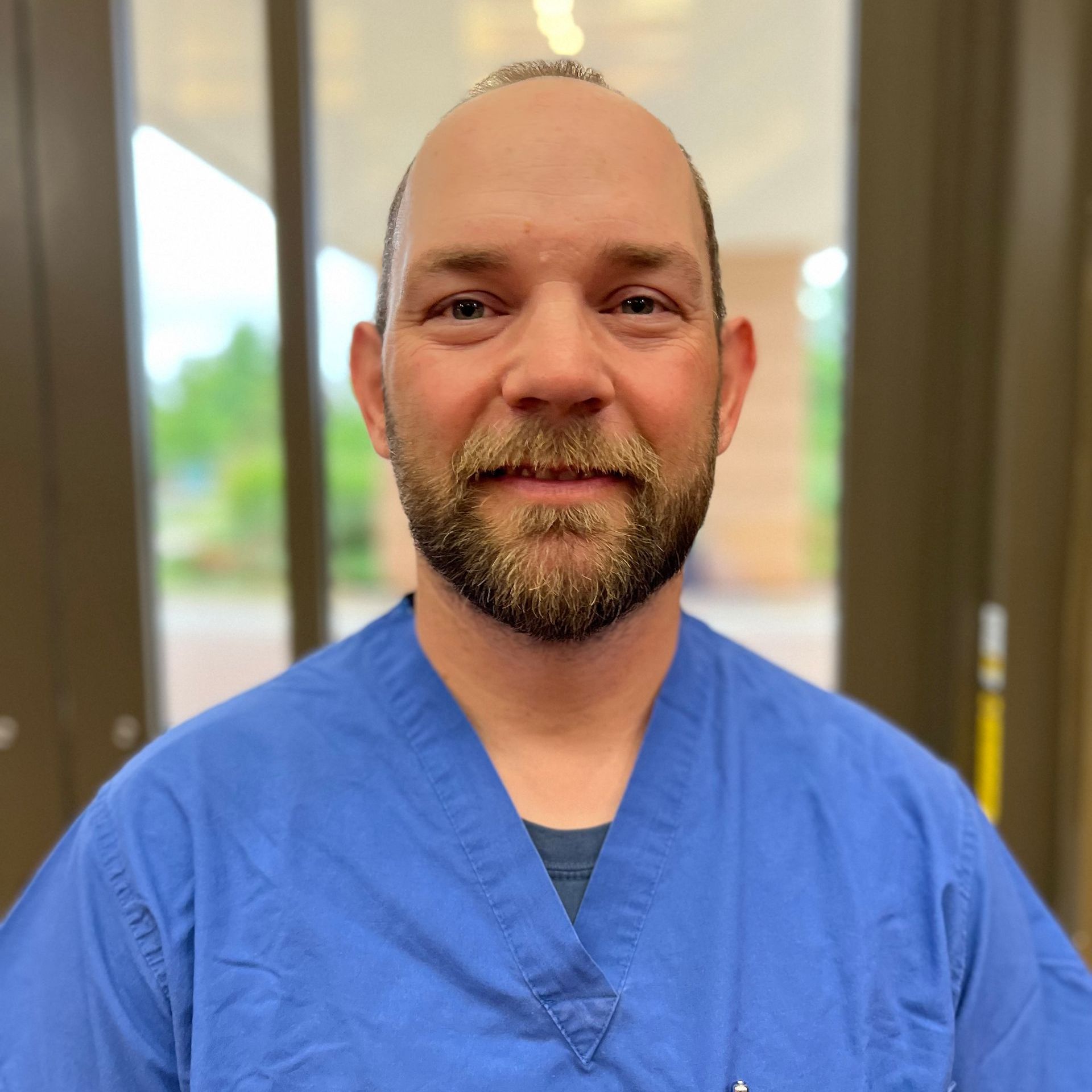 A bald man with a beard wearing a blue scrub top