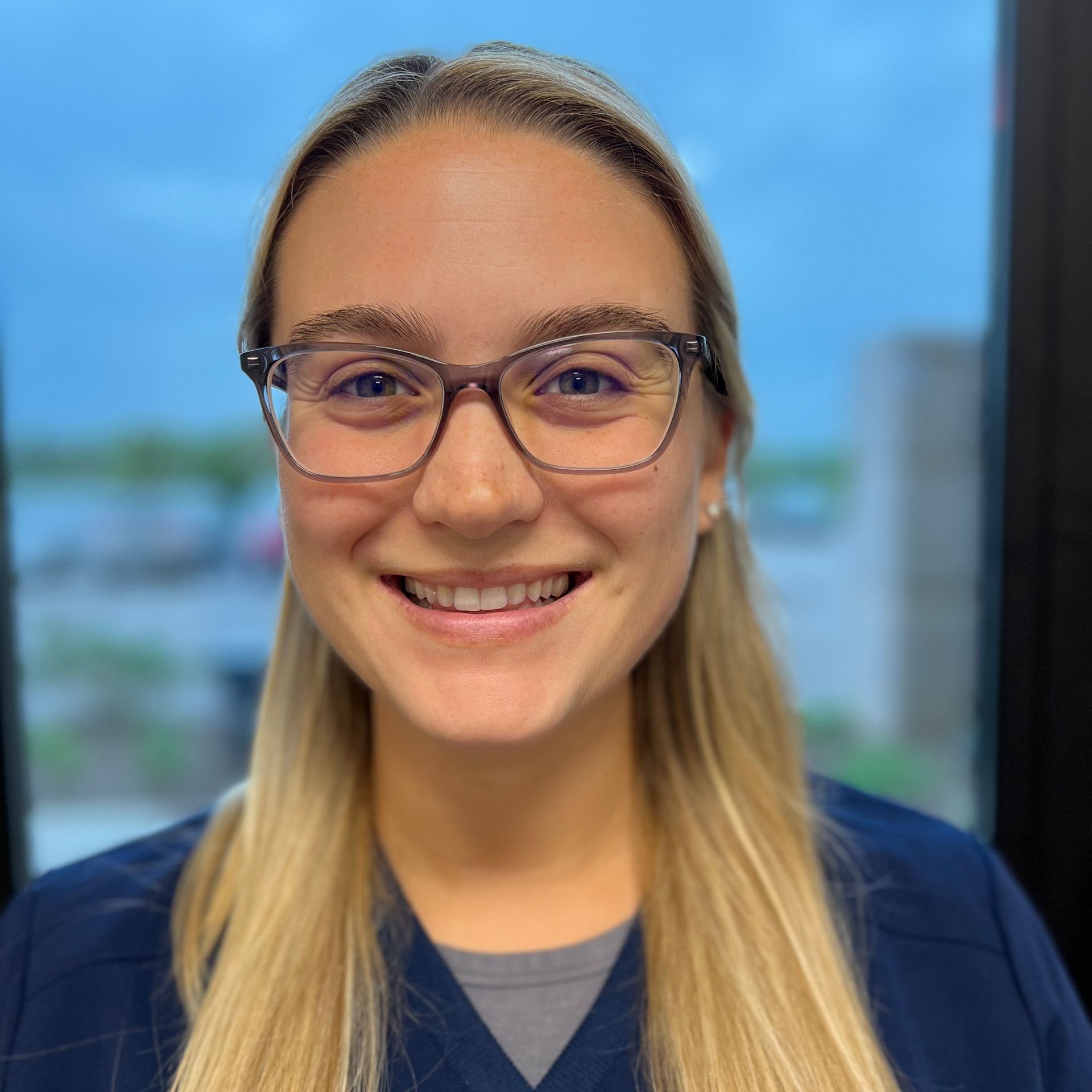 A woman with glasses wearing a navy scrub top.