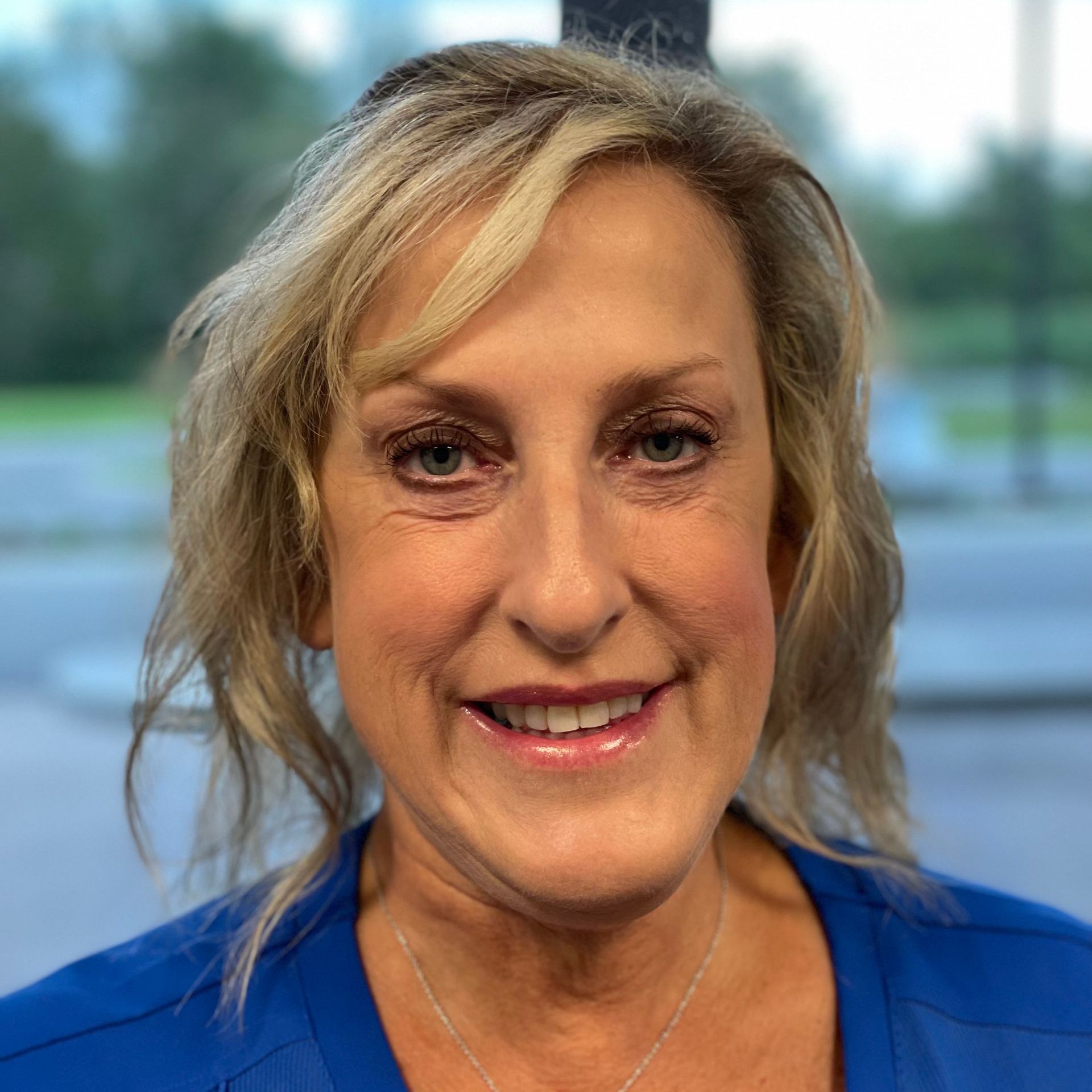 A woman wearing  a blue scrub top smiles for the camera.
