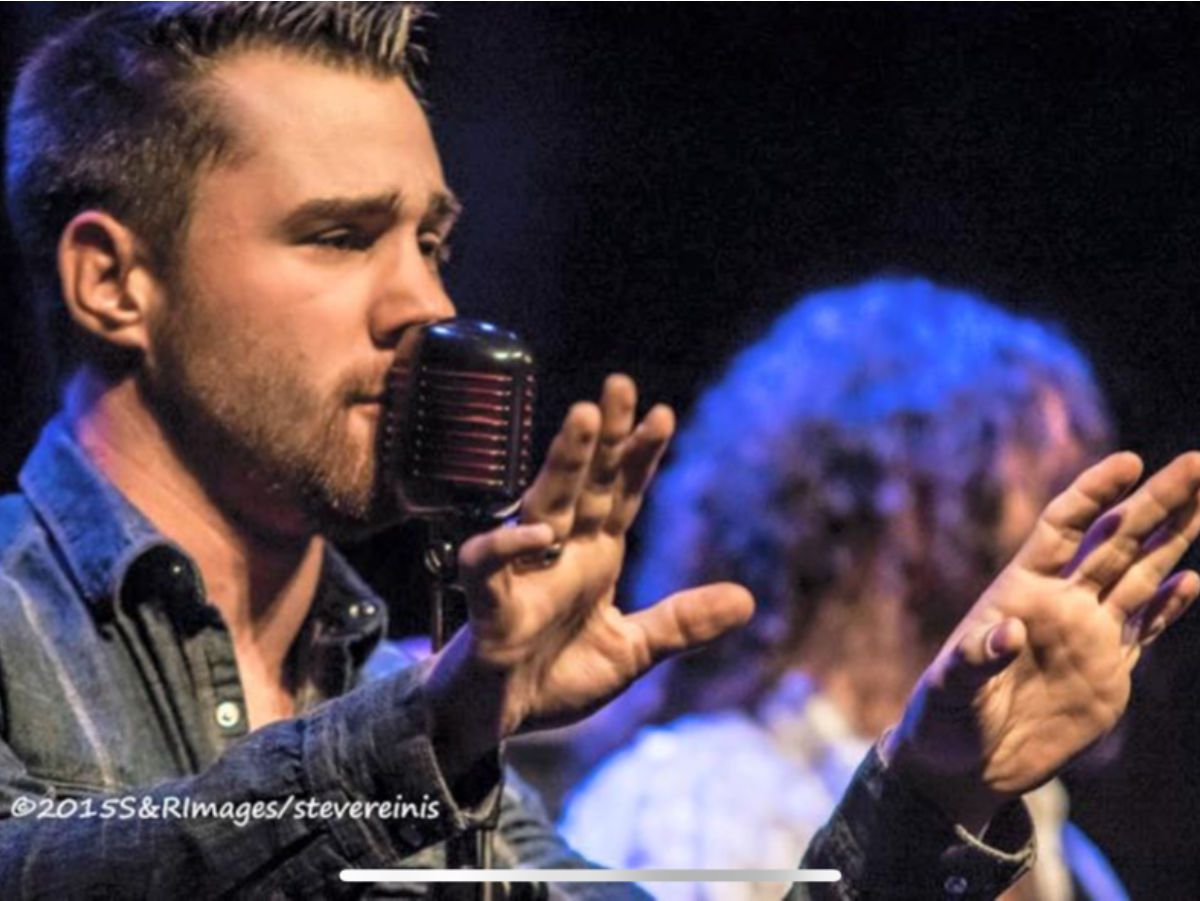 A man singing into a microphone with his hands in the air