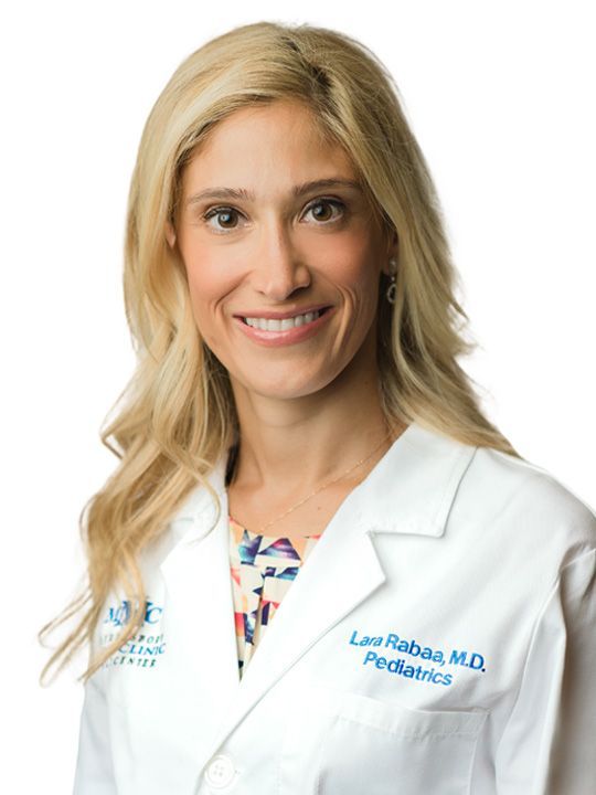 A woman in a white lab coat is smiling for the camera.